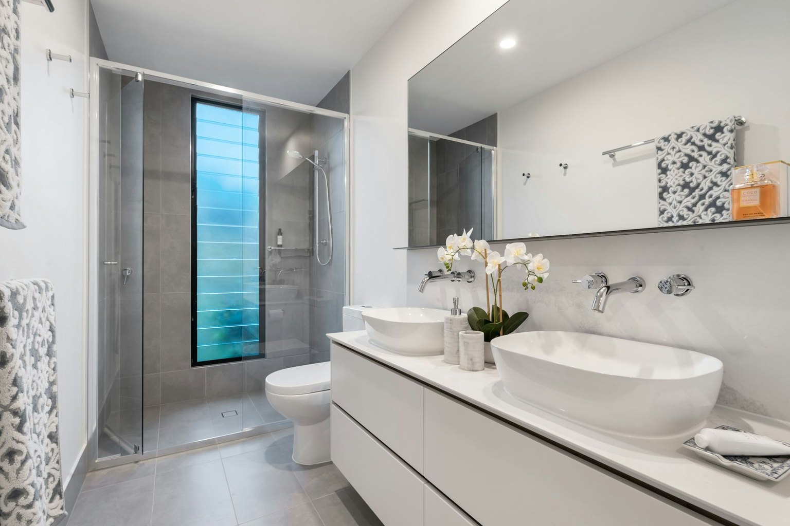Salle d'eau équipée : cabine de douche vitrée, colonne de douche et double vasque à poser sur meuble